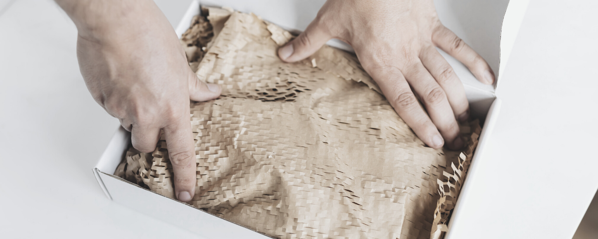 white cardboard box being packed with brown paper